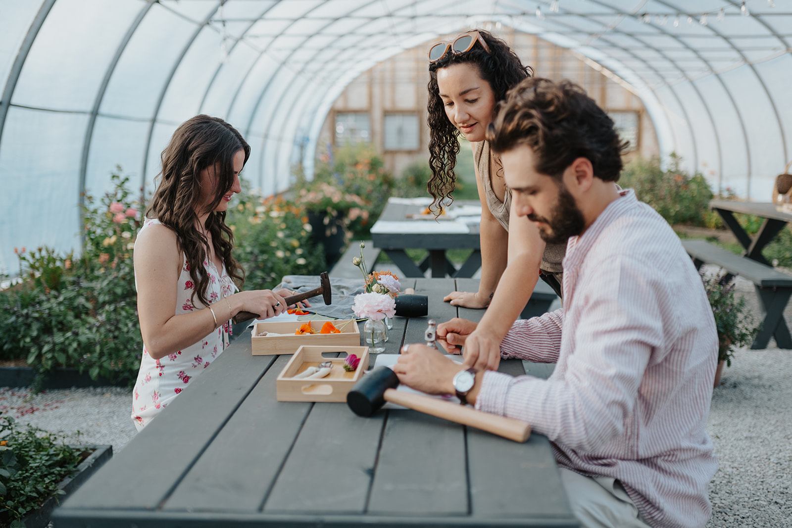 People crafting at a picnic table inside a greenhouse surrounded by flowers.