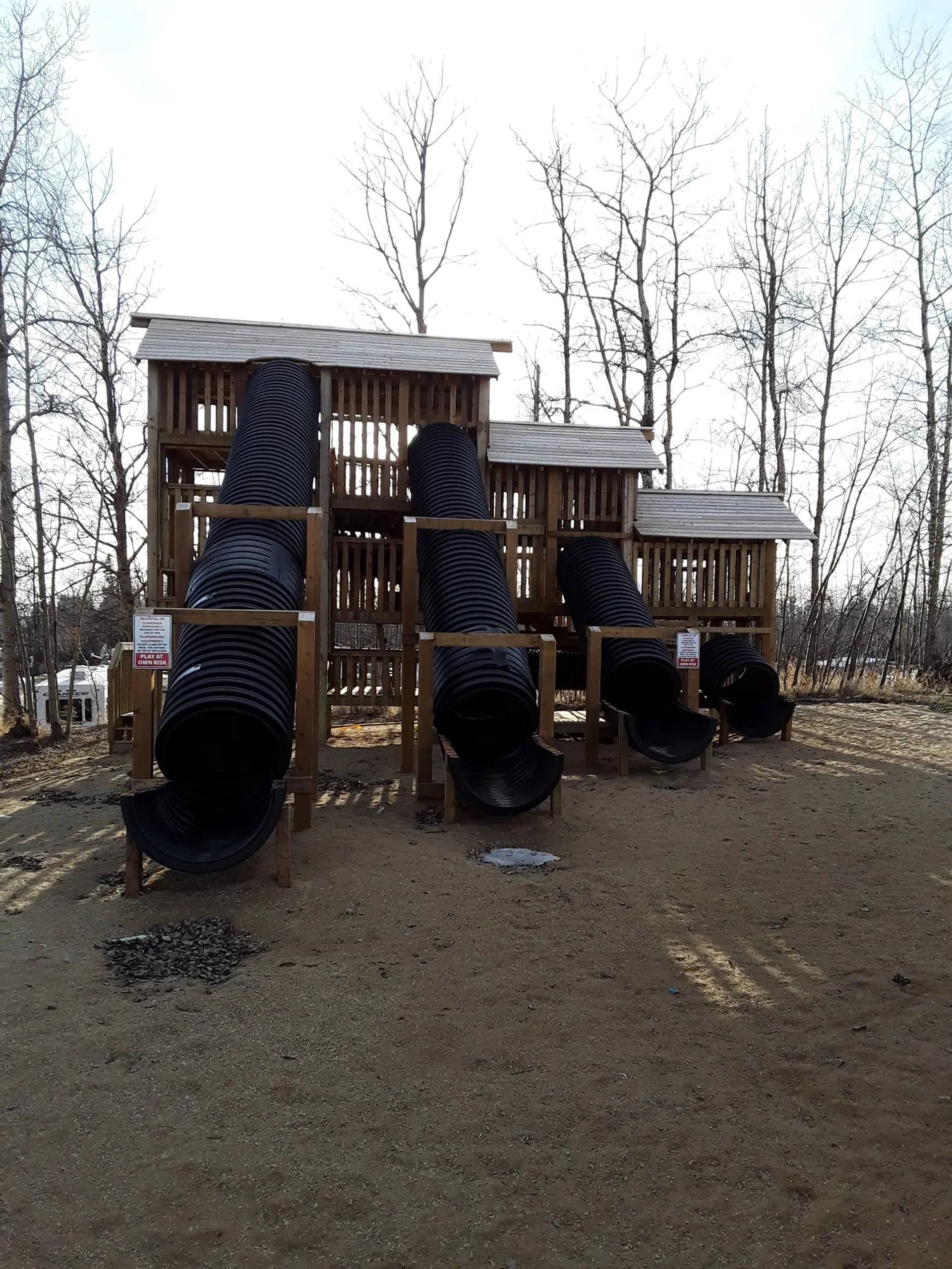 Playground with three black tube slides and wooden platforms outdoors.
