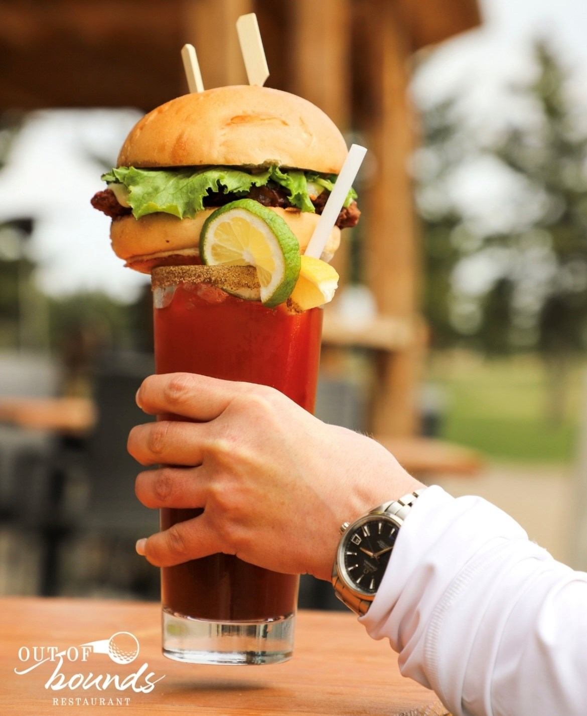 Hand holding a burger in a red cup with a lemon slice and fries garnish.