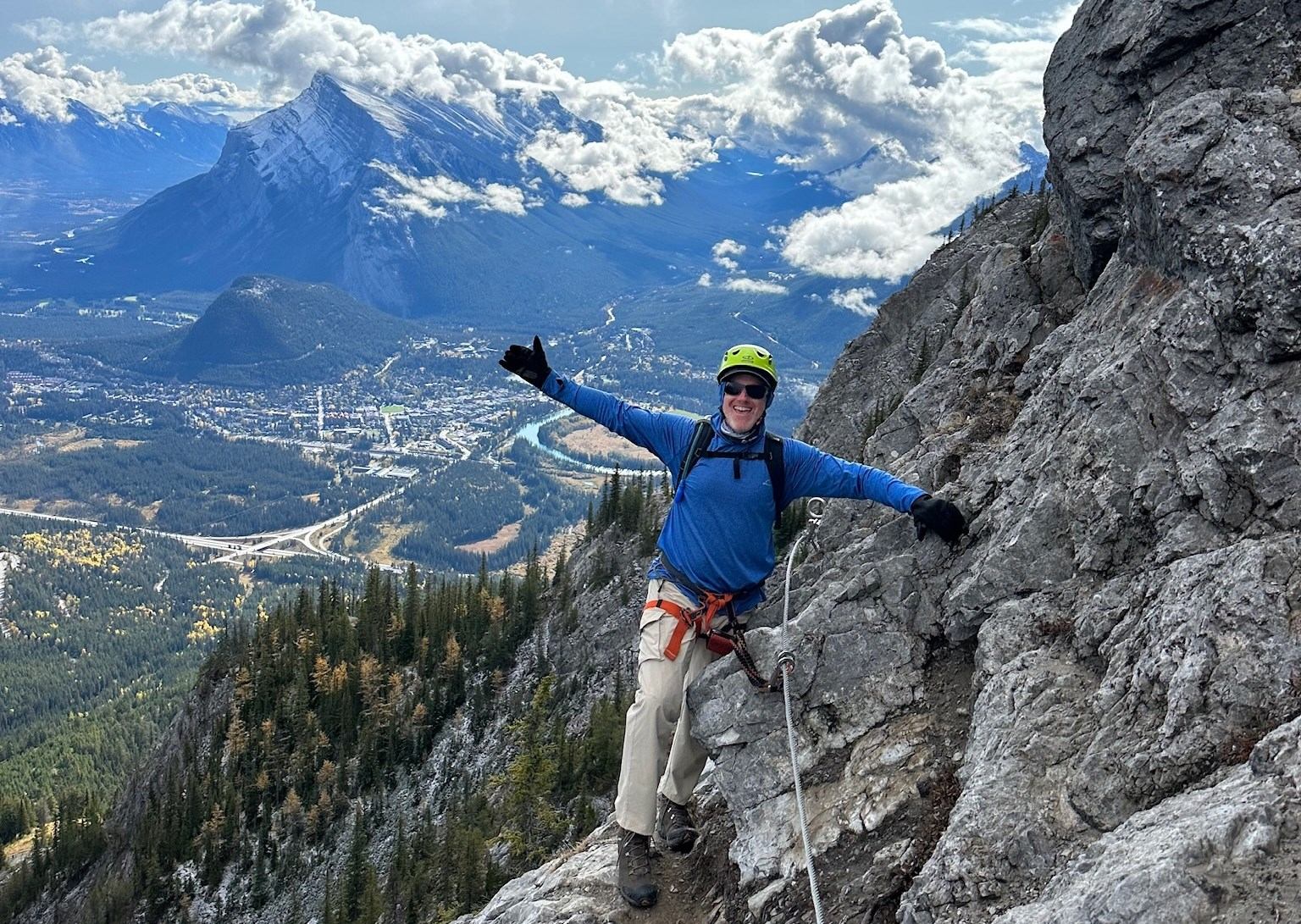 Climber on rocky mountain with scenic valley and peaks in the background.