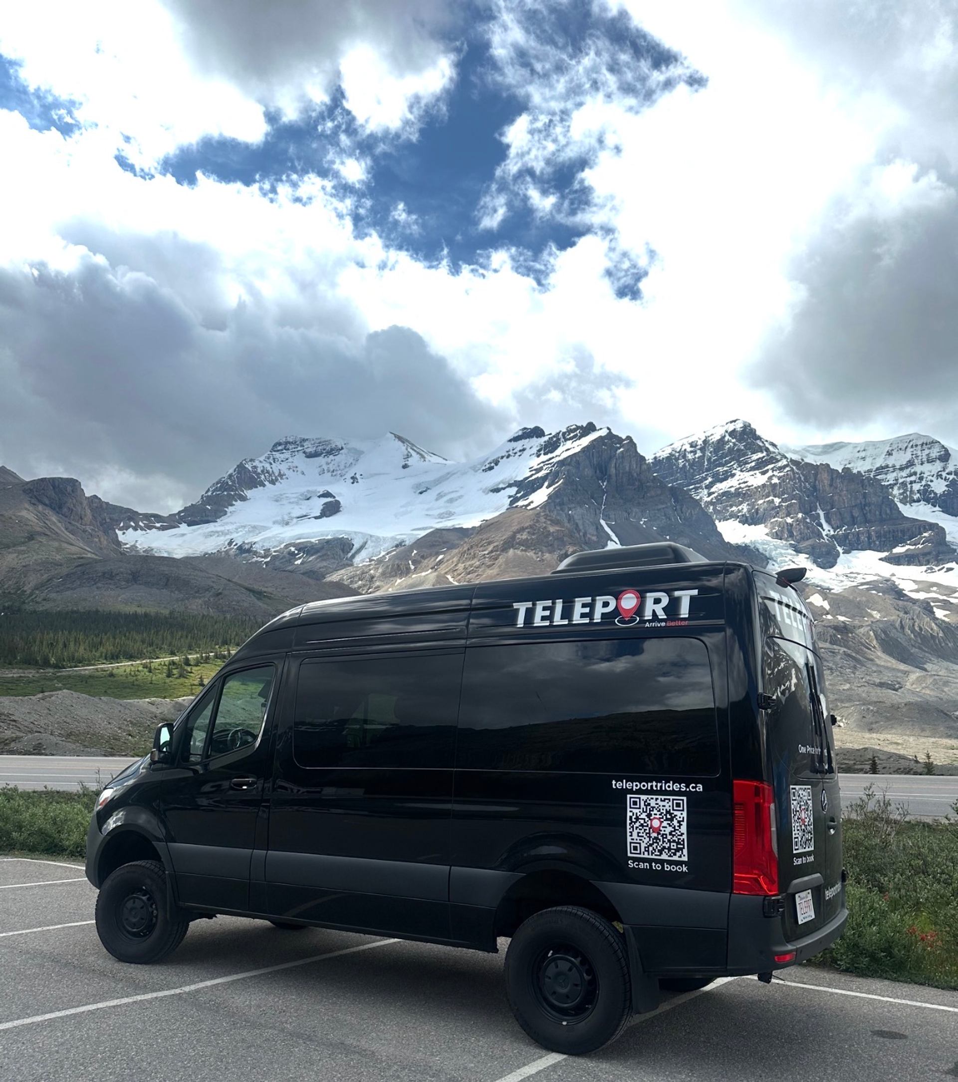 Black TELEPORT van parked by highway with snowy mountain range and cloudy sky.