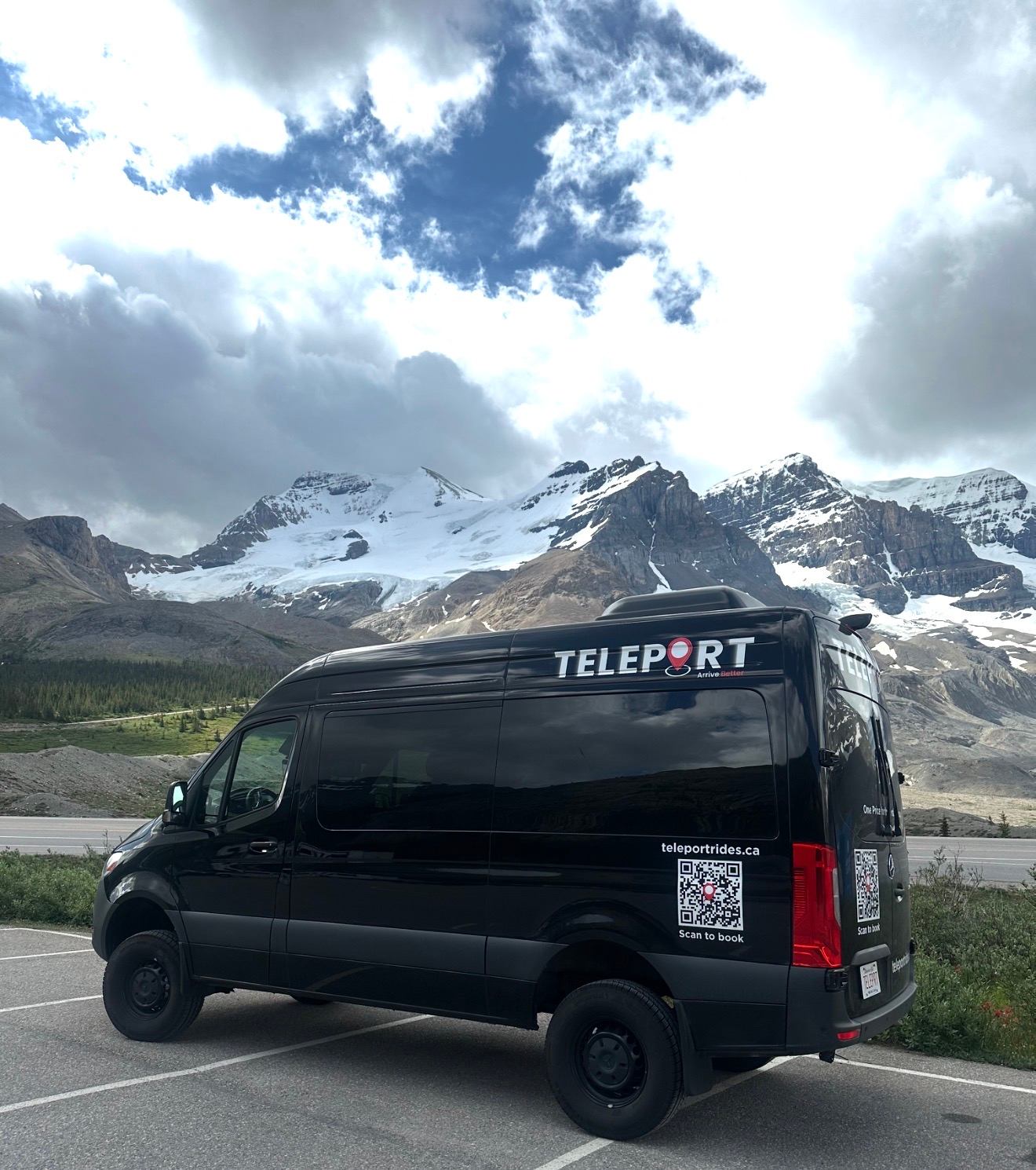 Black TELEPORT van parked by highway with snowy mountain range and cloudy sky.