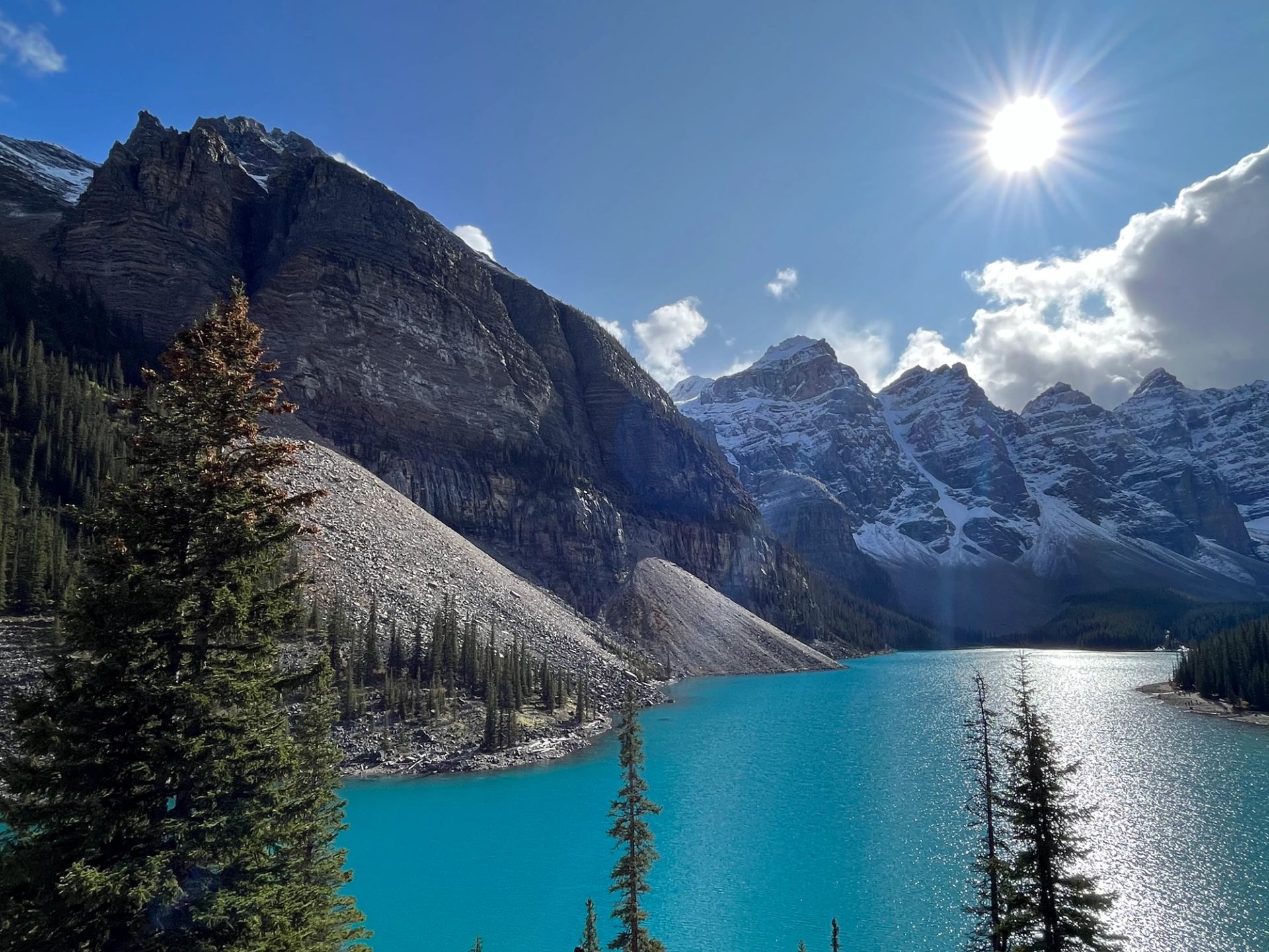 Bright turquoise Moraine Lake with sunlit peaks and evergreen trees.
