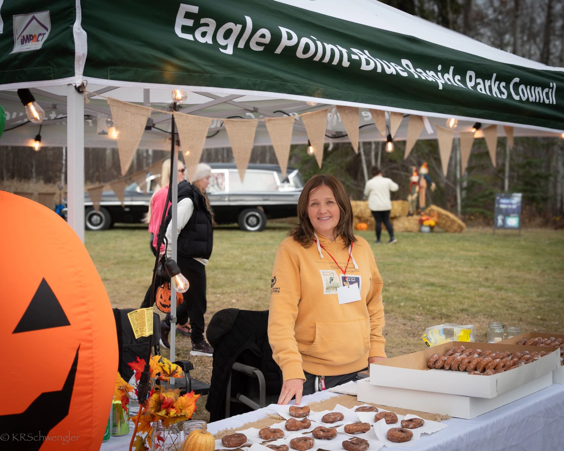 Vendor at Eagle Point-Blue Rapids Parks Council booth selling donuts at outdoor event.