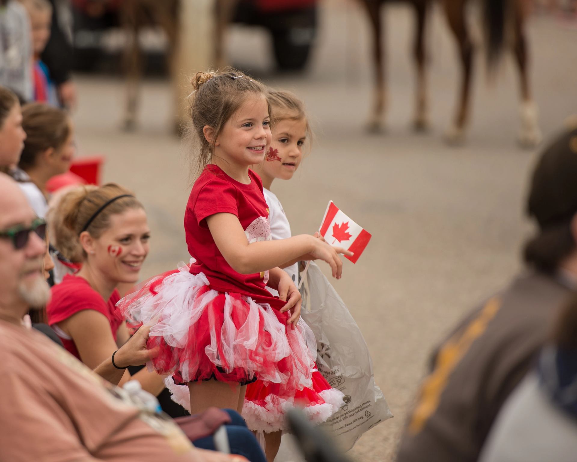 Children in red and white outfits hold a small Canadian flag at a parade.