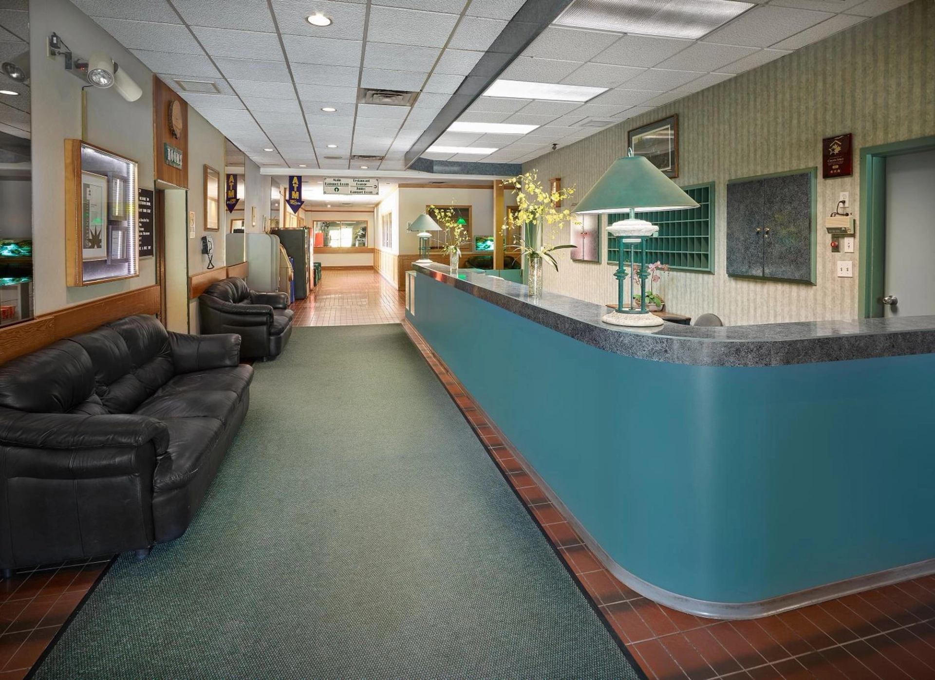 A long teal reception desk in a hotel lobby with black leather couches and a hallway in the background.