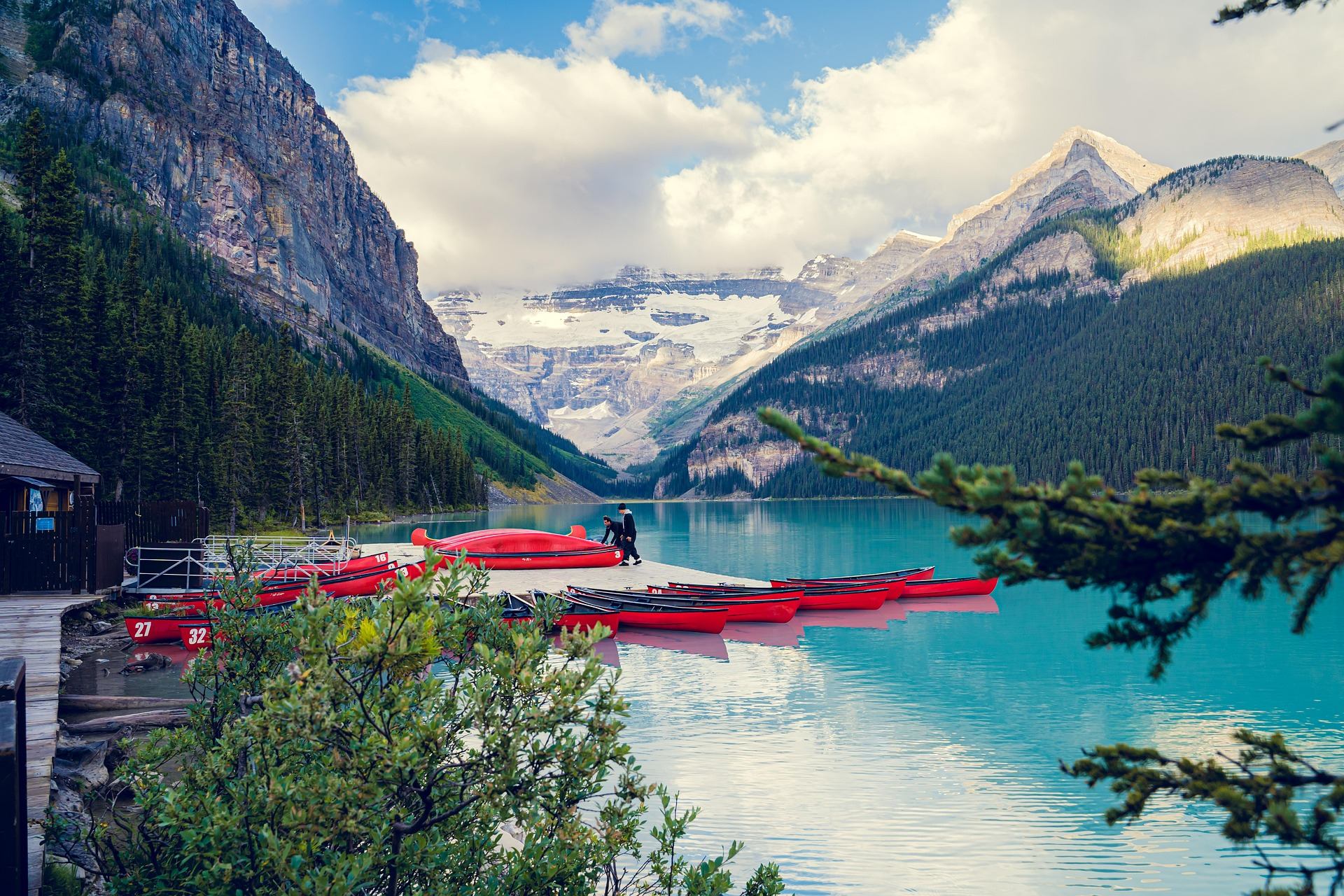 Turquoise mountain lake with red canoes at dock, surrounded by forested cliffs and glaciers.