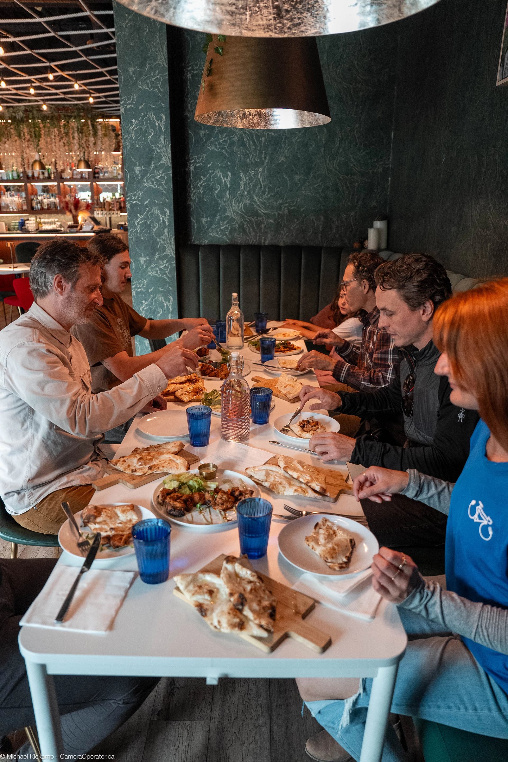 Group dining at The Roaring Rolls with plates of food, blue glasses, and warm pendant lighting overhead.