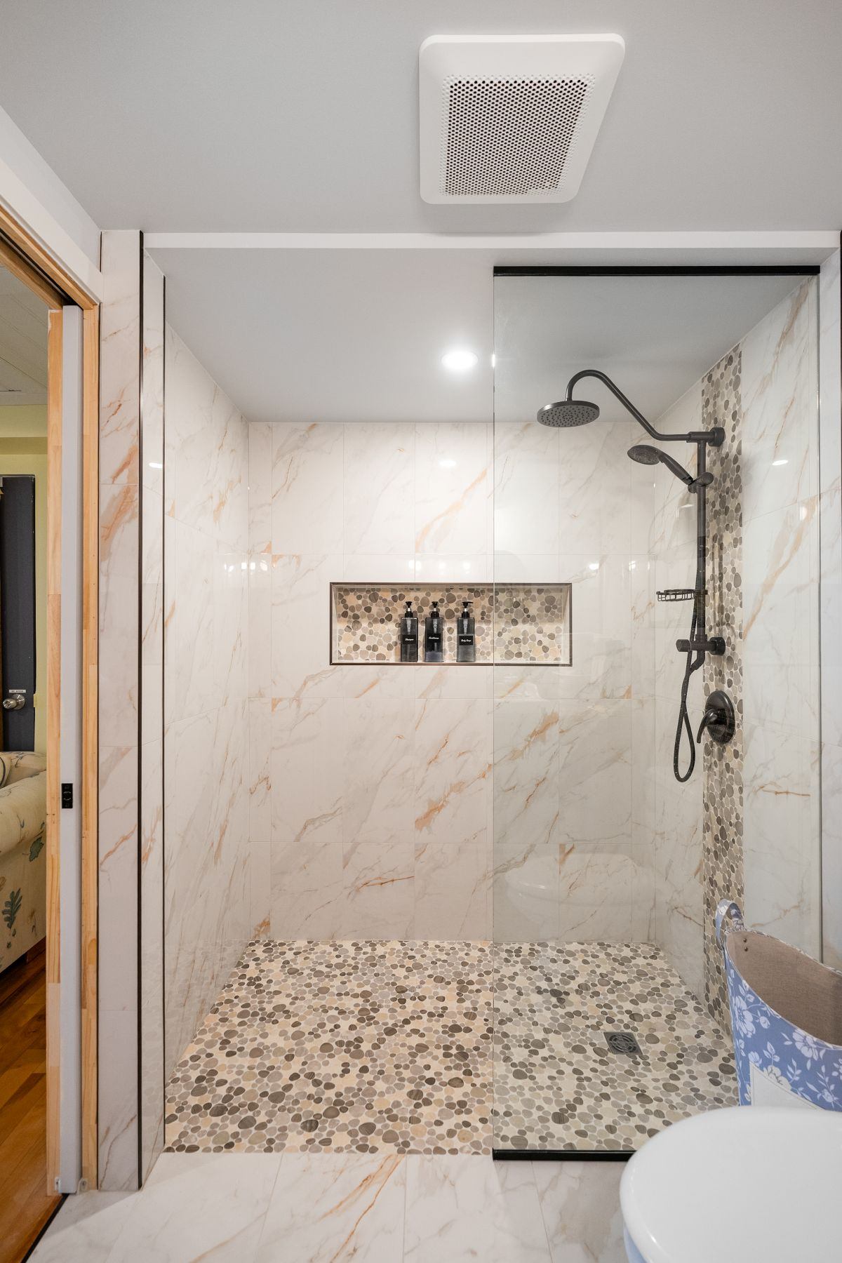 Modern walk-in shower with marble walls and pebble floor.