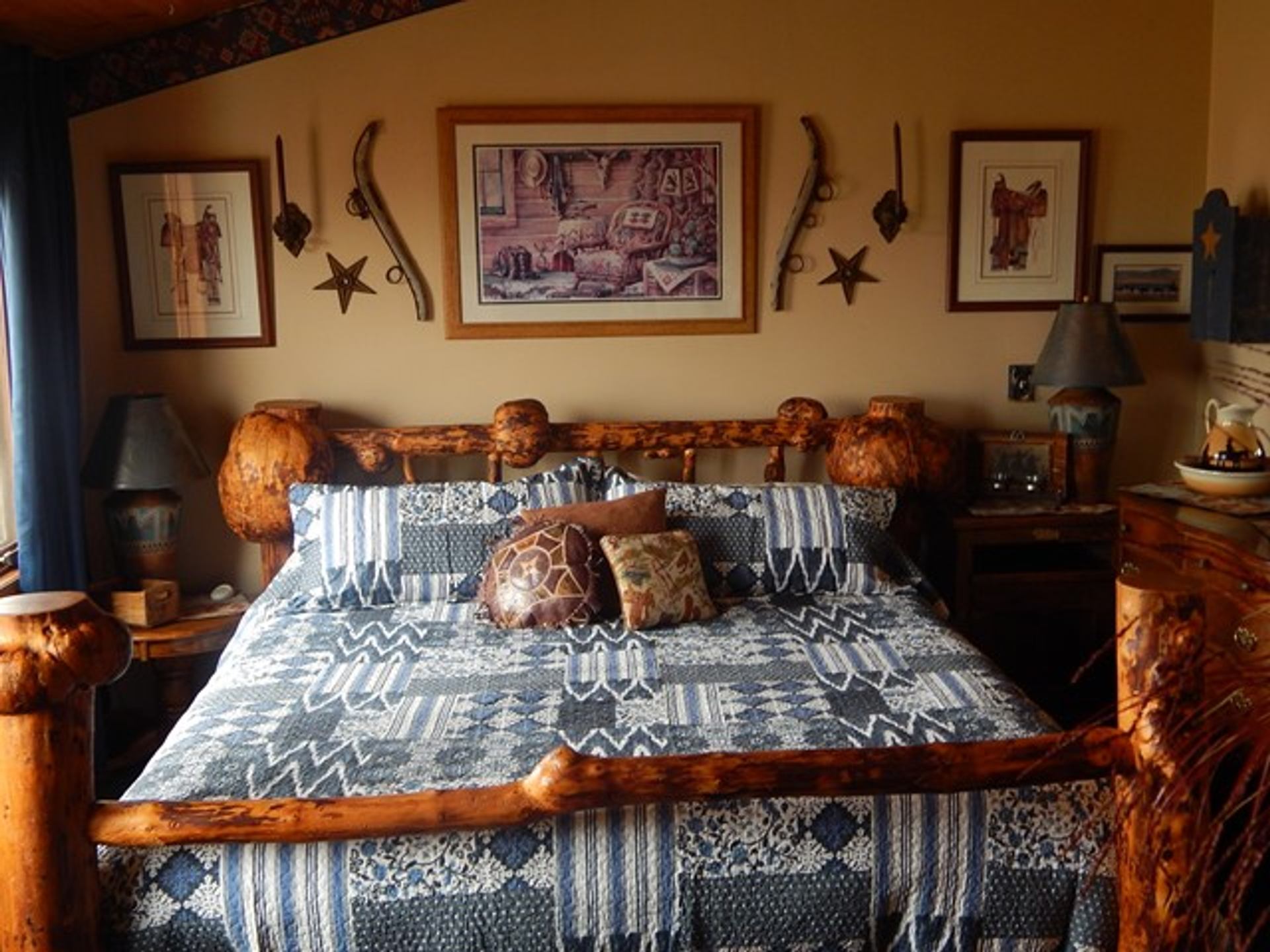 Log-frame bed with patterned quilt, lamps and western wall art in bedroom.