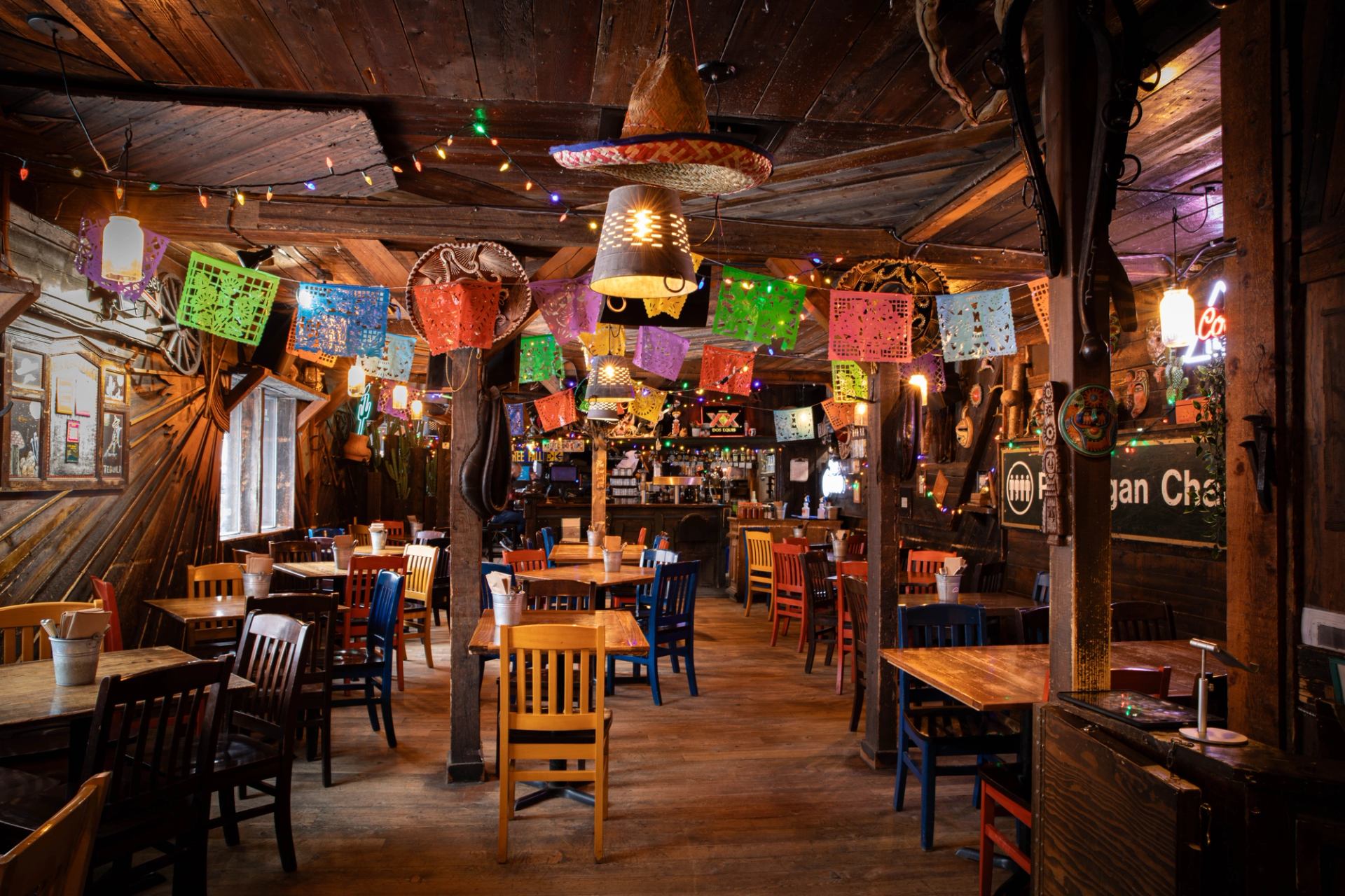 Rustic restaurant interior decorated with colorful papel picado, string lights, and sombreros.