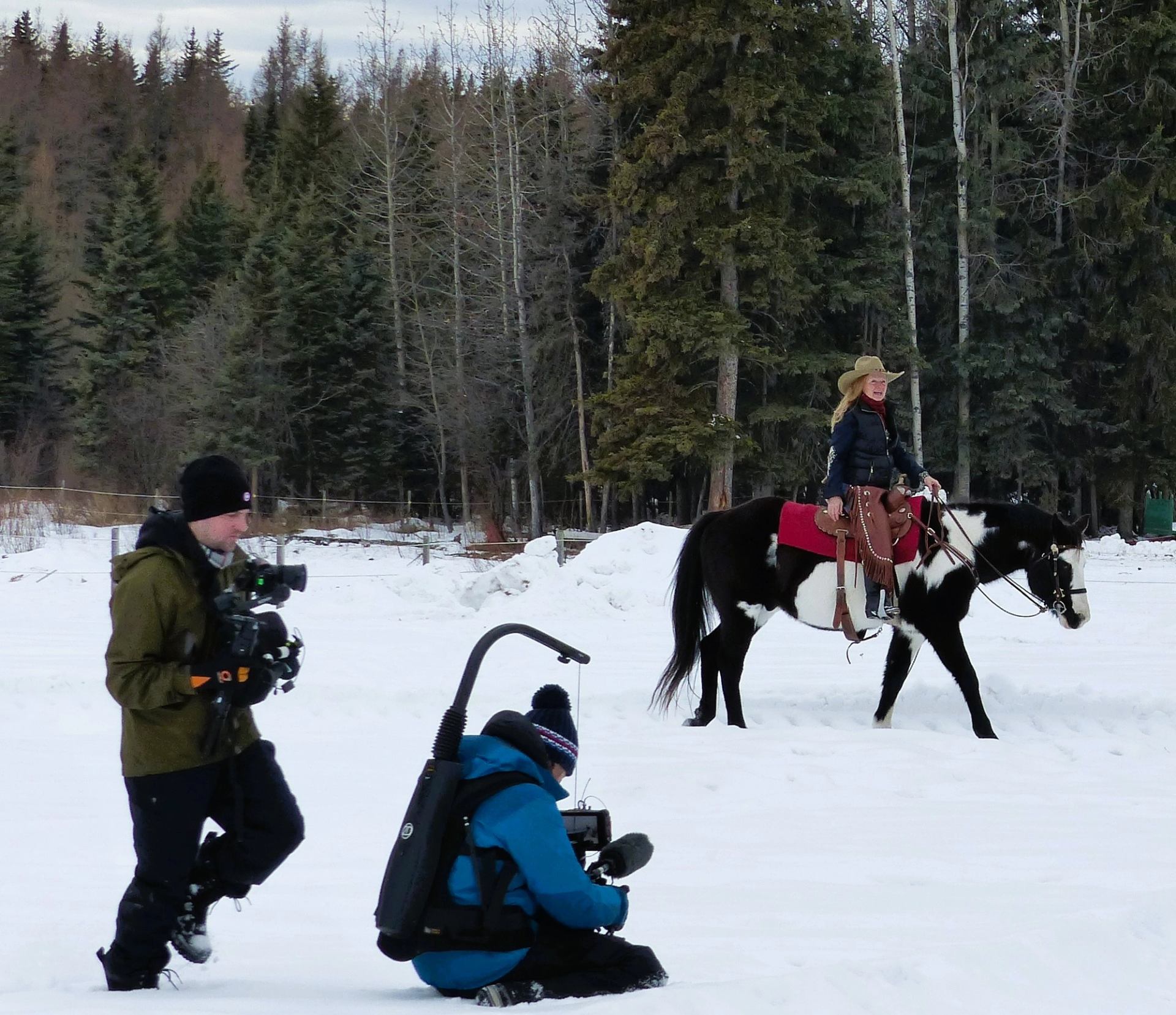 Horse and rider moving through snowy ground with film crew nearby
