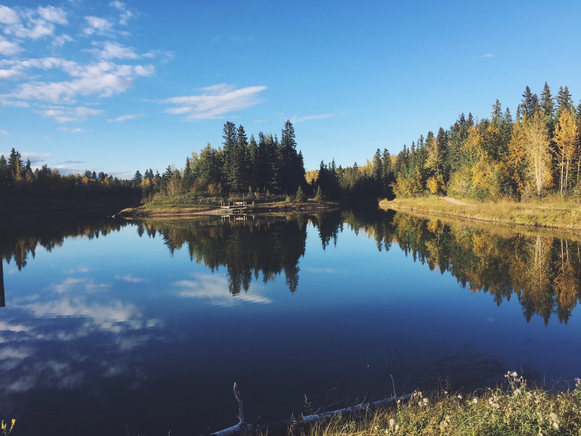 Calm lake reflecting autumn trees and sky in a peaceful ranch setting.
