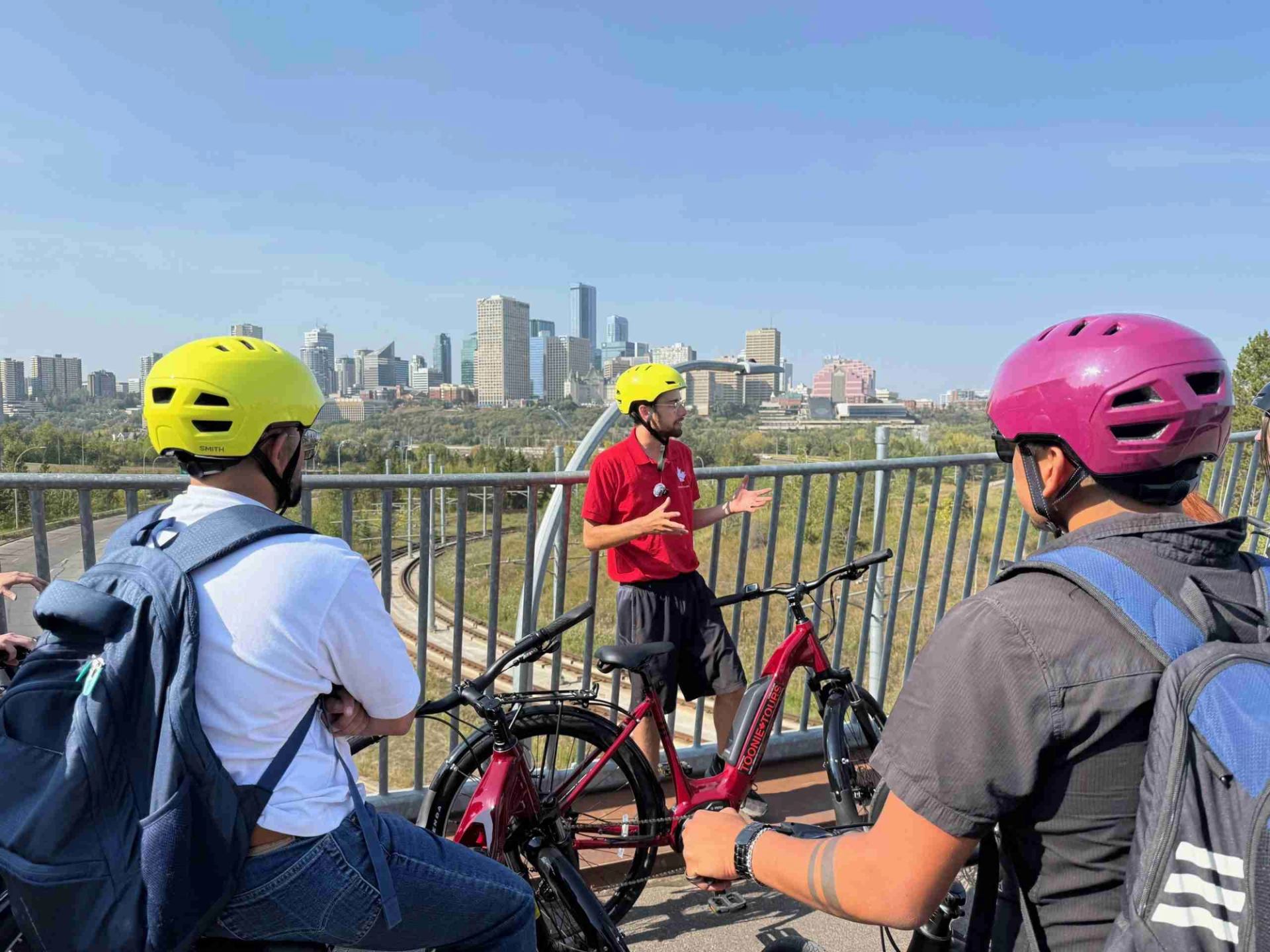 A tour guide speaks to cyclists on a bridge overlooking Edmonton's downtown skyline and river valley.