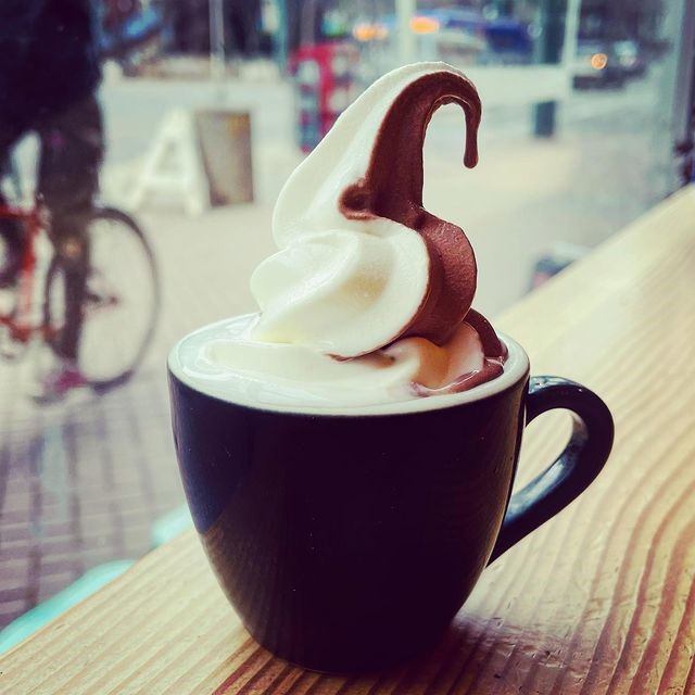 Black cup filled with espresso topped with swirled vanilla and chocolate soft‑serve.