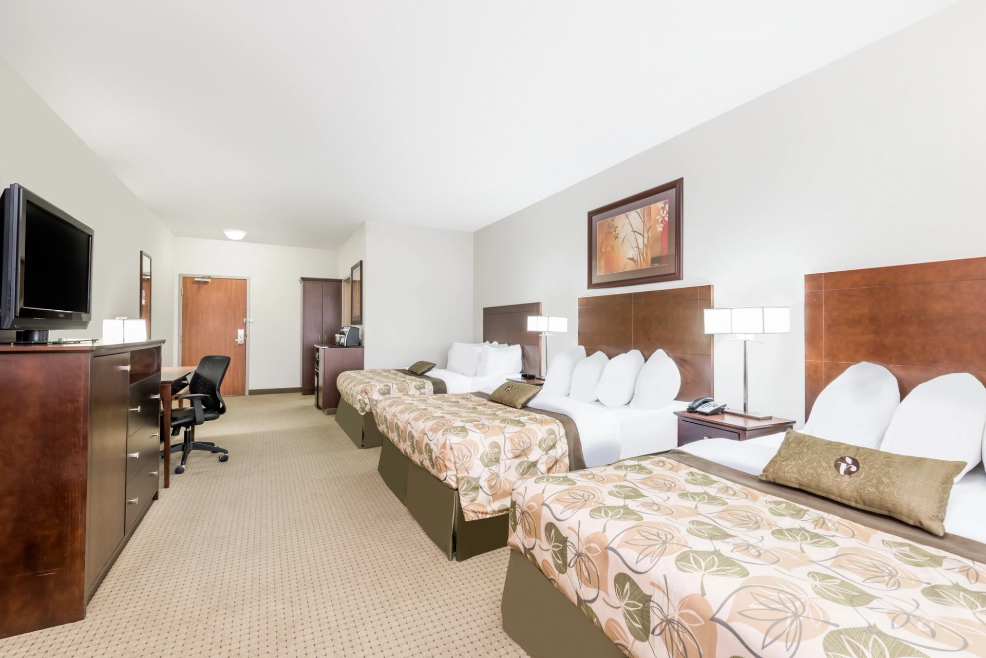 Hotel room with two beds, desk, office chair, television and wooden furniture.