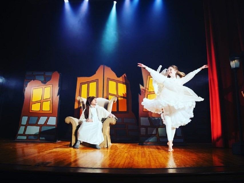 Performer leaps mid-air on stage with lit buildings in the backdrop.