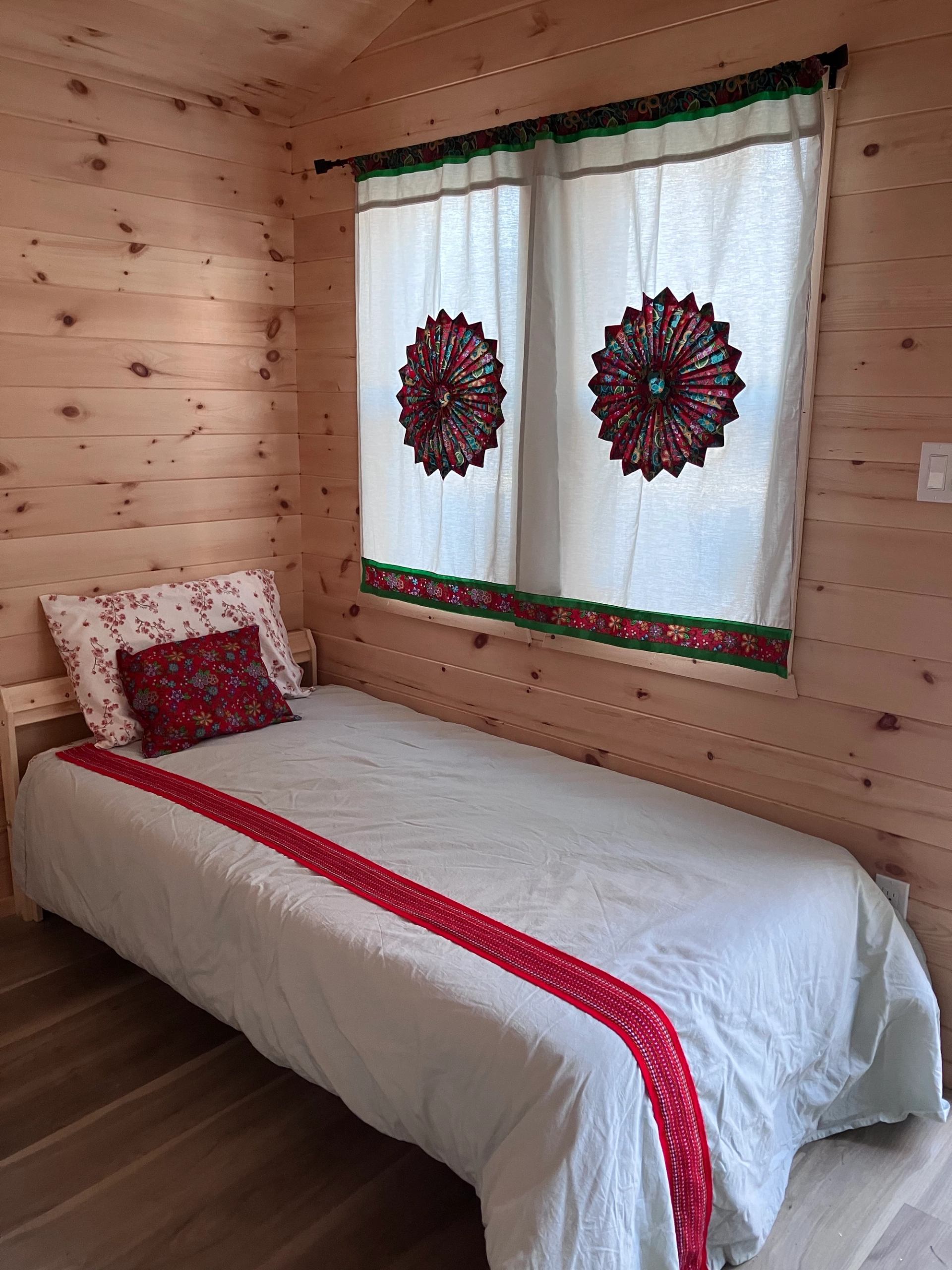 Single bed with white and red bedding and decorative curtains in a wooden cabin
