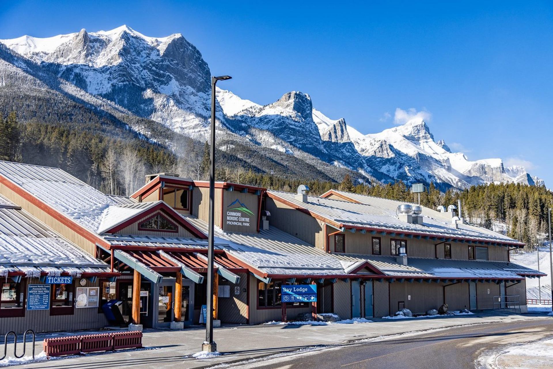 Snow-covered lodge at Canmore Nordic Centre with majestic snow-capped mountains in the background.