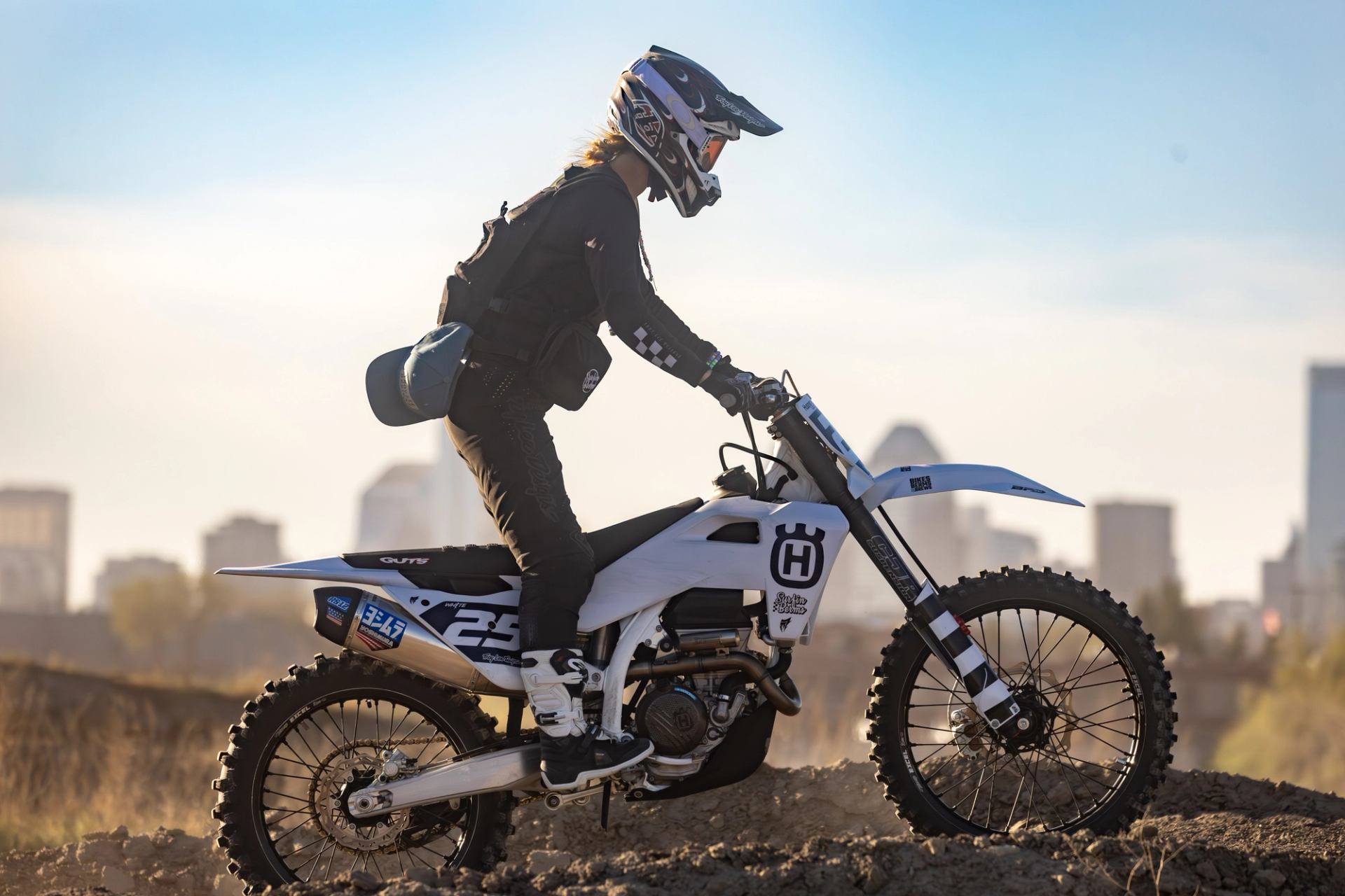 Rider on white dirt bike #25 with city skyline in the background.