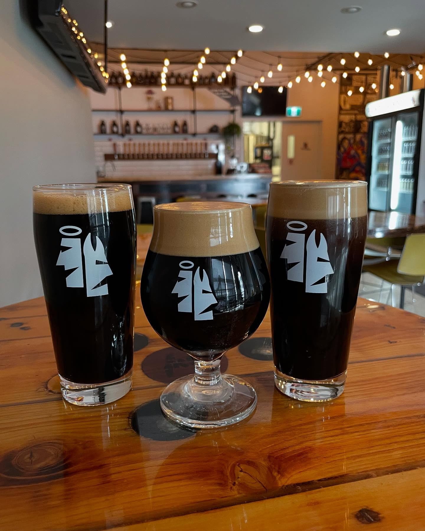 Three dark beers on a wooden table inside the Omen Brewing taproom