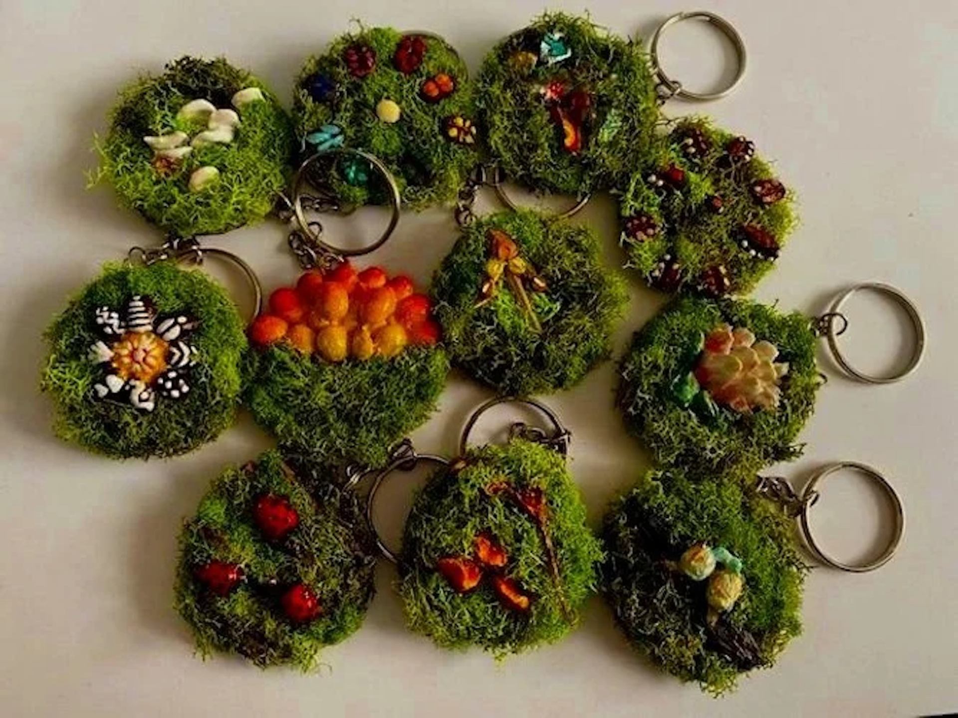 Handmade mossy keychains with mini mushrooms, berries, and floral decorations.