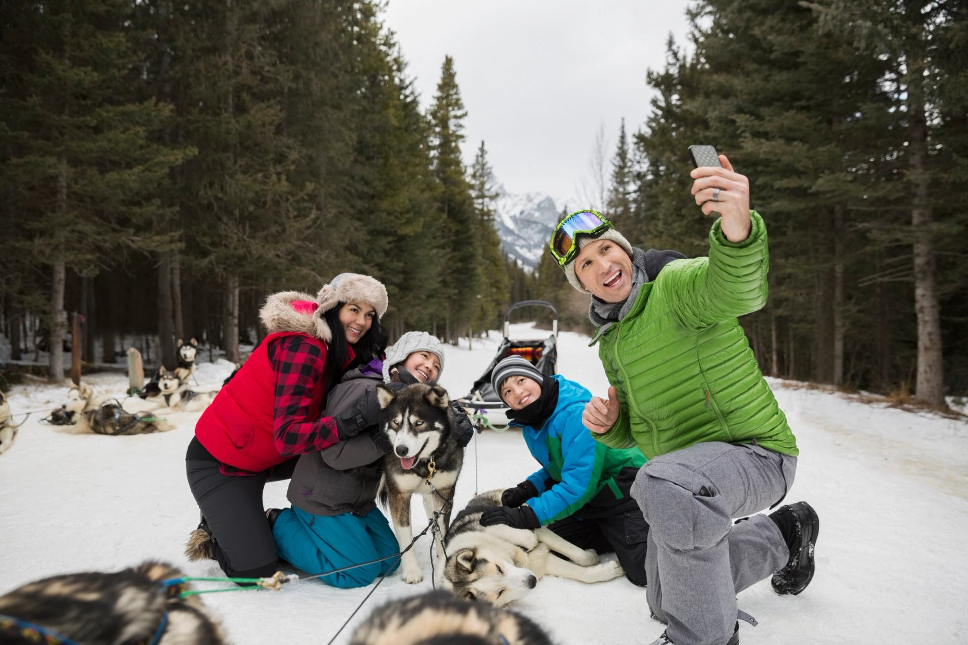Group taking a selfie with friendly sled dogs on a snowy Banff trail.