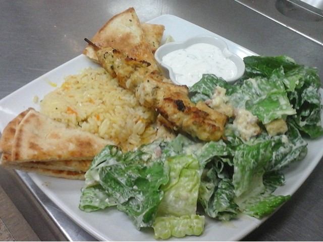 Greek platter with chicken skewer, rice, pita, salad, and tzatziki sauce.