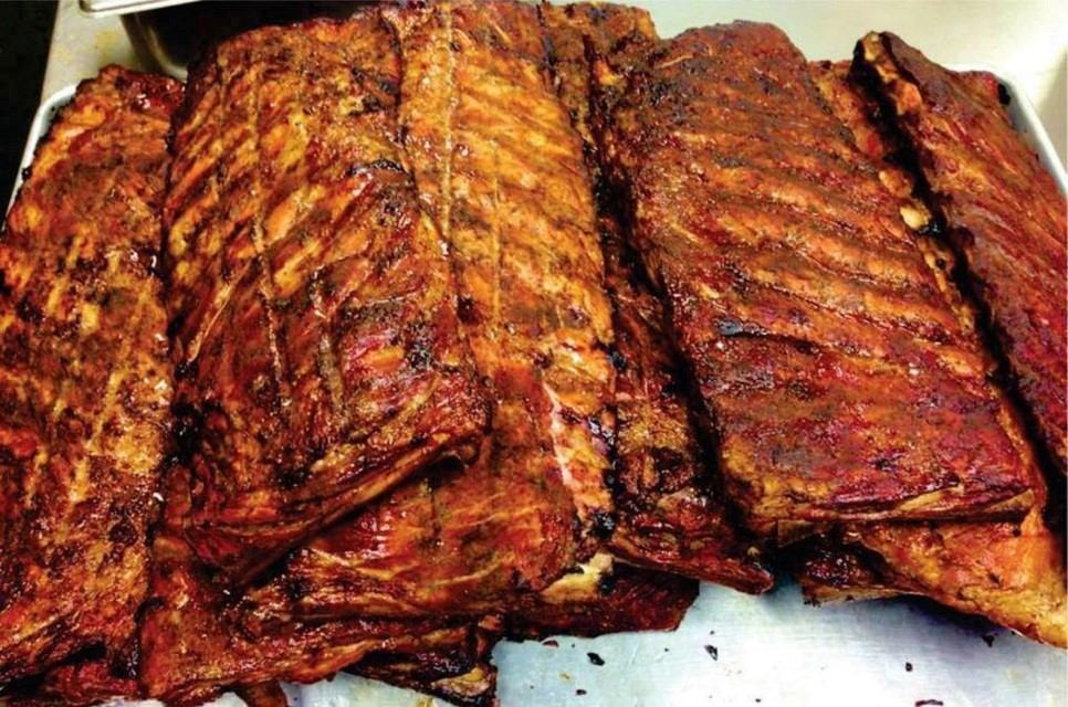 Multiple racks of cooked, seasoned ribs on a metal tray.