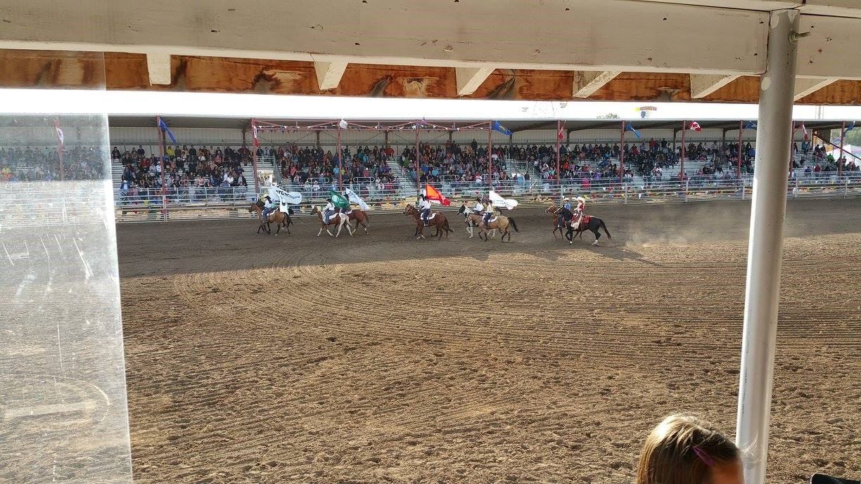 Rodeo arena with riders on horseback in an outdoor arena, surrounded by bleachers.