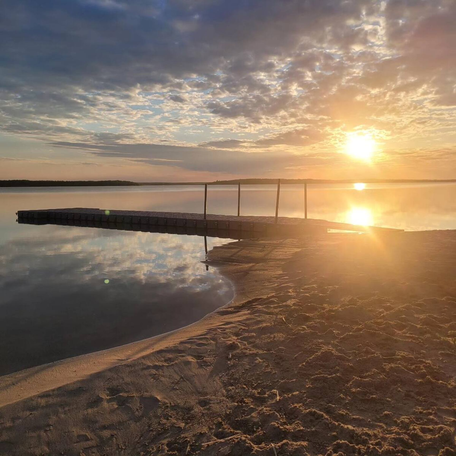 A calm lake at sunset with golden light reflecting off the water and sandy shore.
