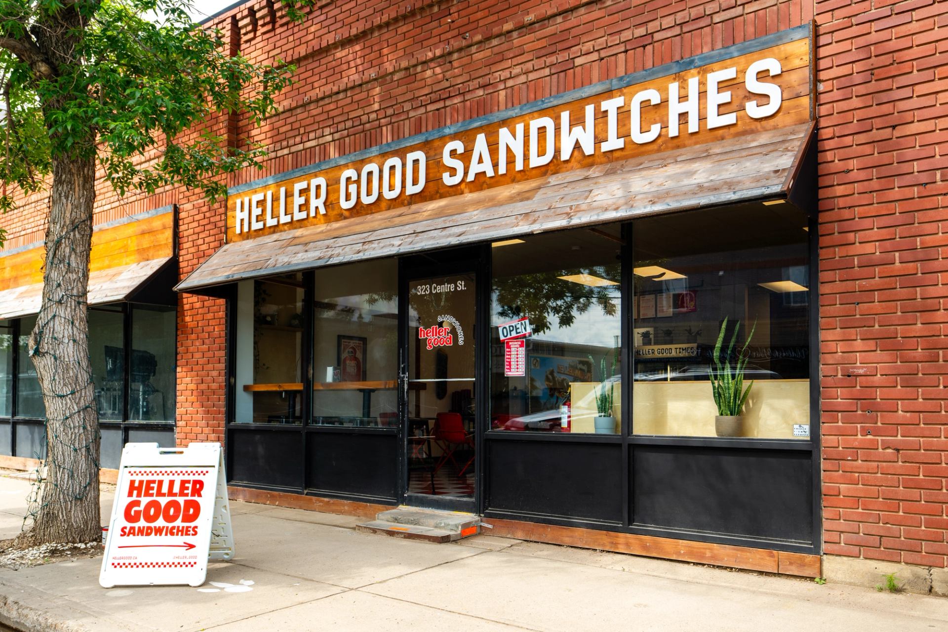 Storefront of "Heller Good Sandwiches" shop with a wooden sign and an A-frame on the sidewalk.