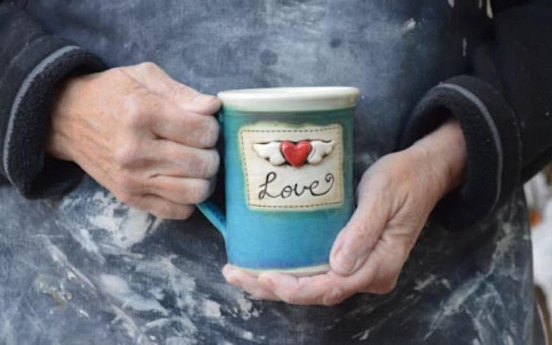 Hands holding a blue mug with red heart, wings and the word Love.