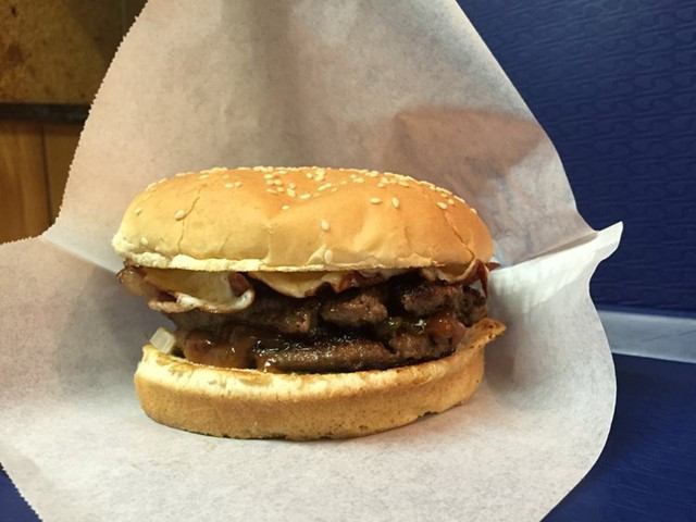 Bacon burger with sesame bun, beef patty, onions, and sauce on parchment paper.