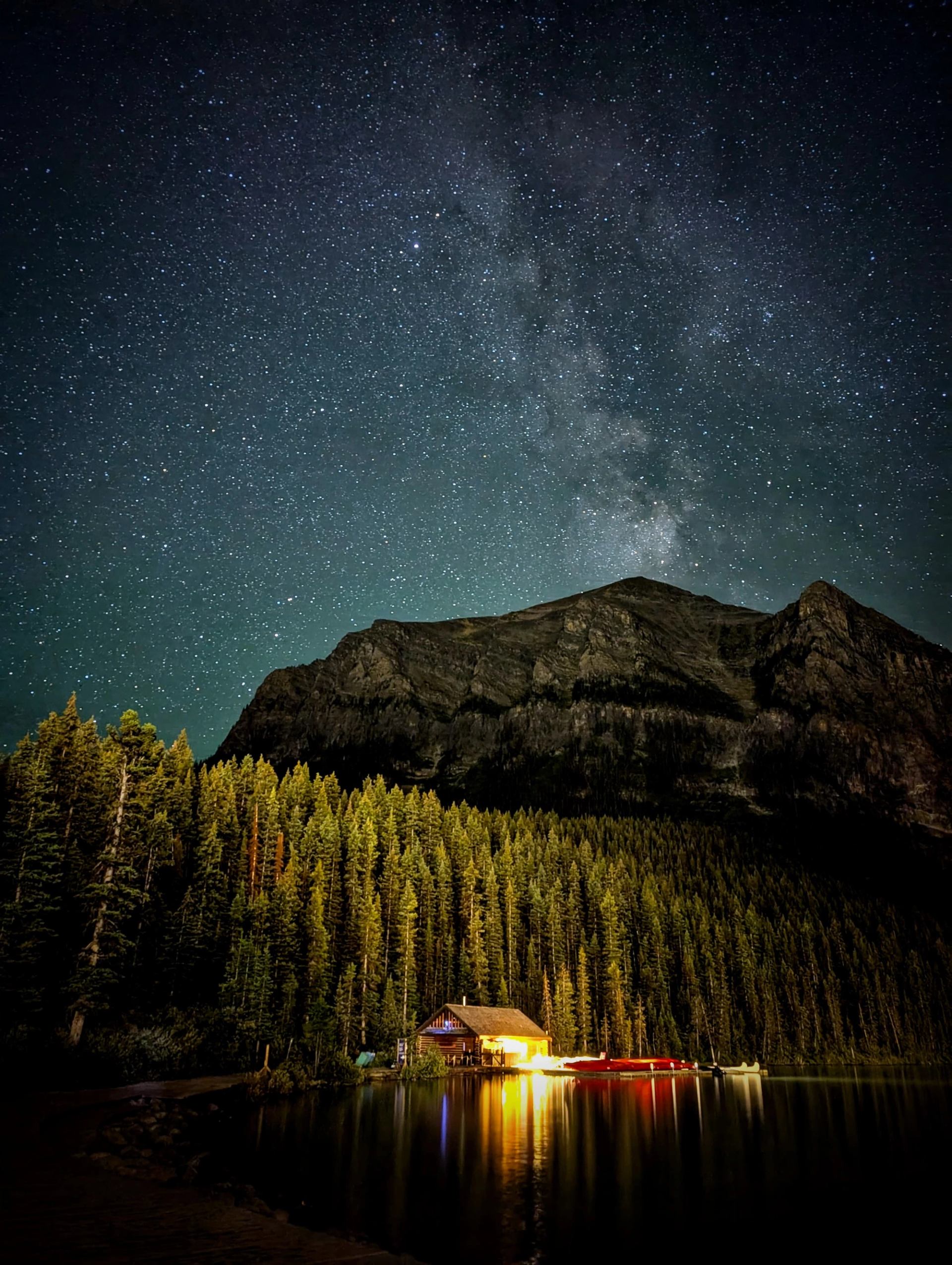 Milky Way shining above a lakeside cabin and forest at Moraine Lake.