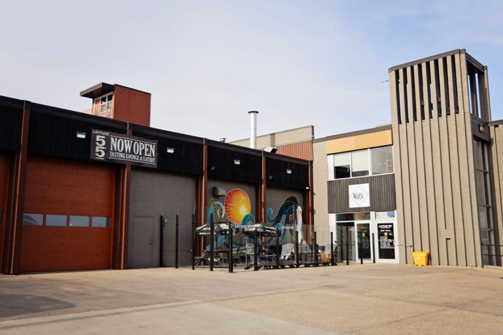Front view of Latitude 55 Distillery with patio seating and a colorful mural.