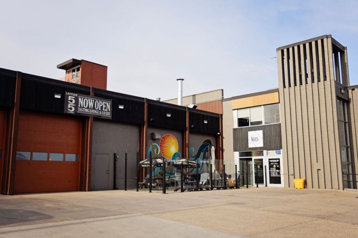 Front view of Latitude 55 Distillery with patio seating and a colorful mural.