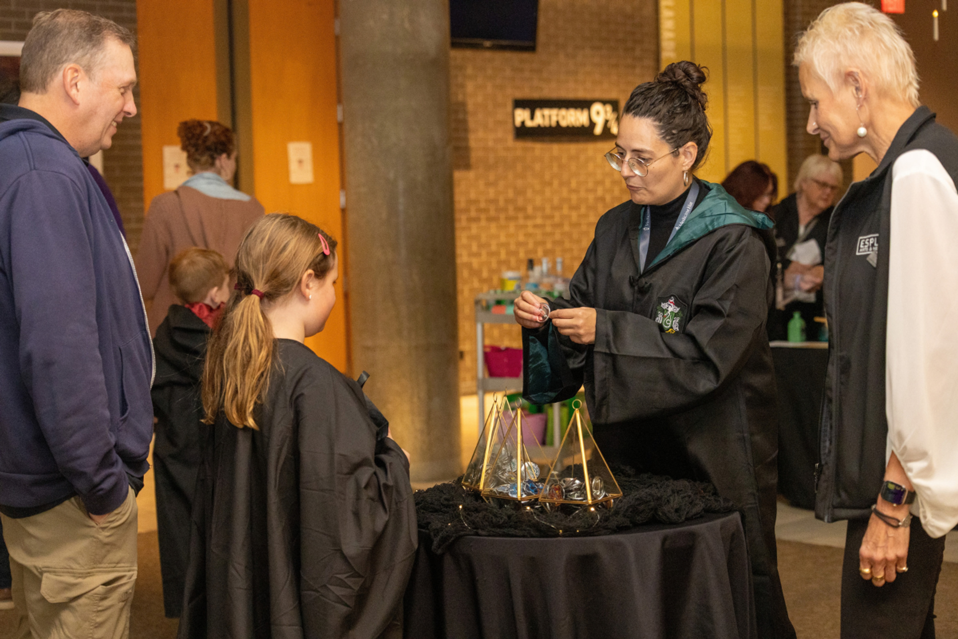 Costumed attendant shows a small item to visitors gathered around a decorated table.