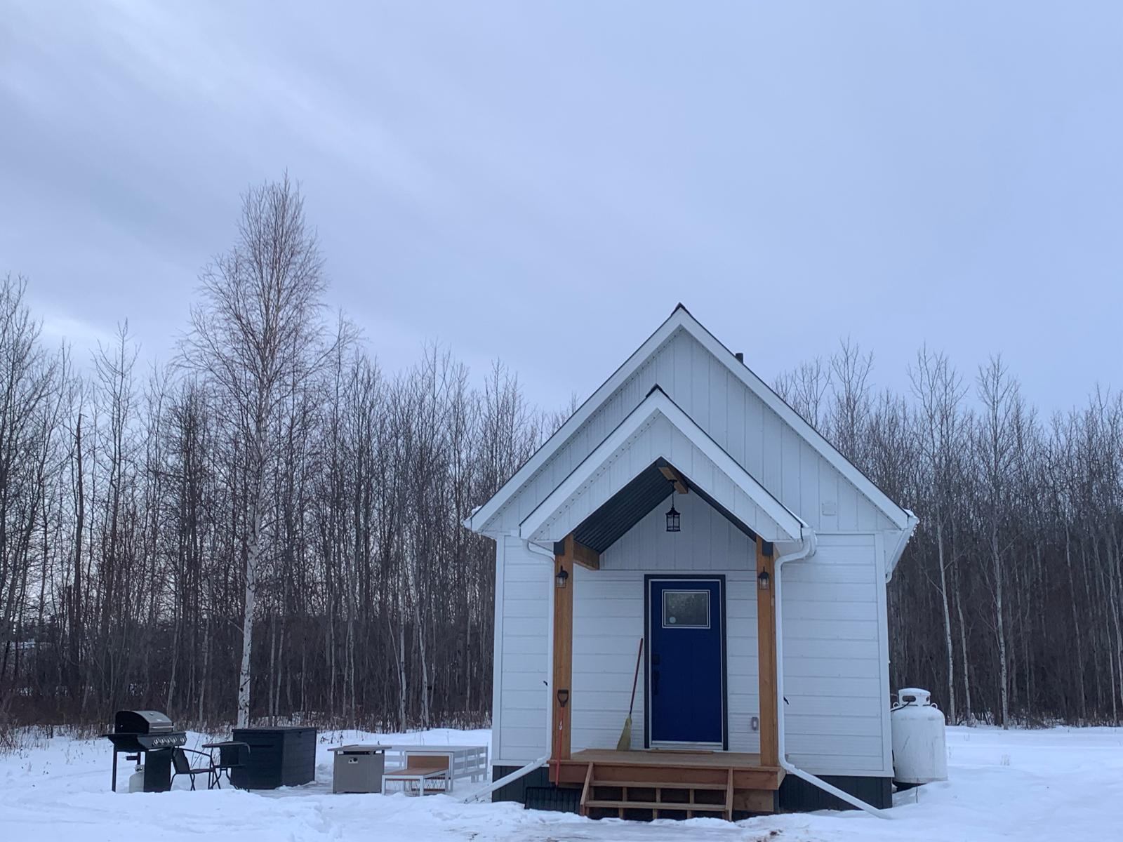 White cabin in snowy woods at Wildly Eweneek Cabins.