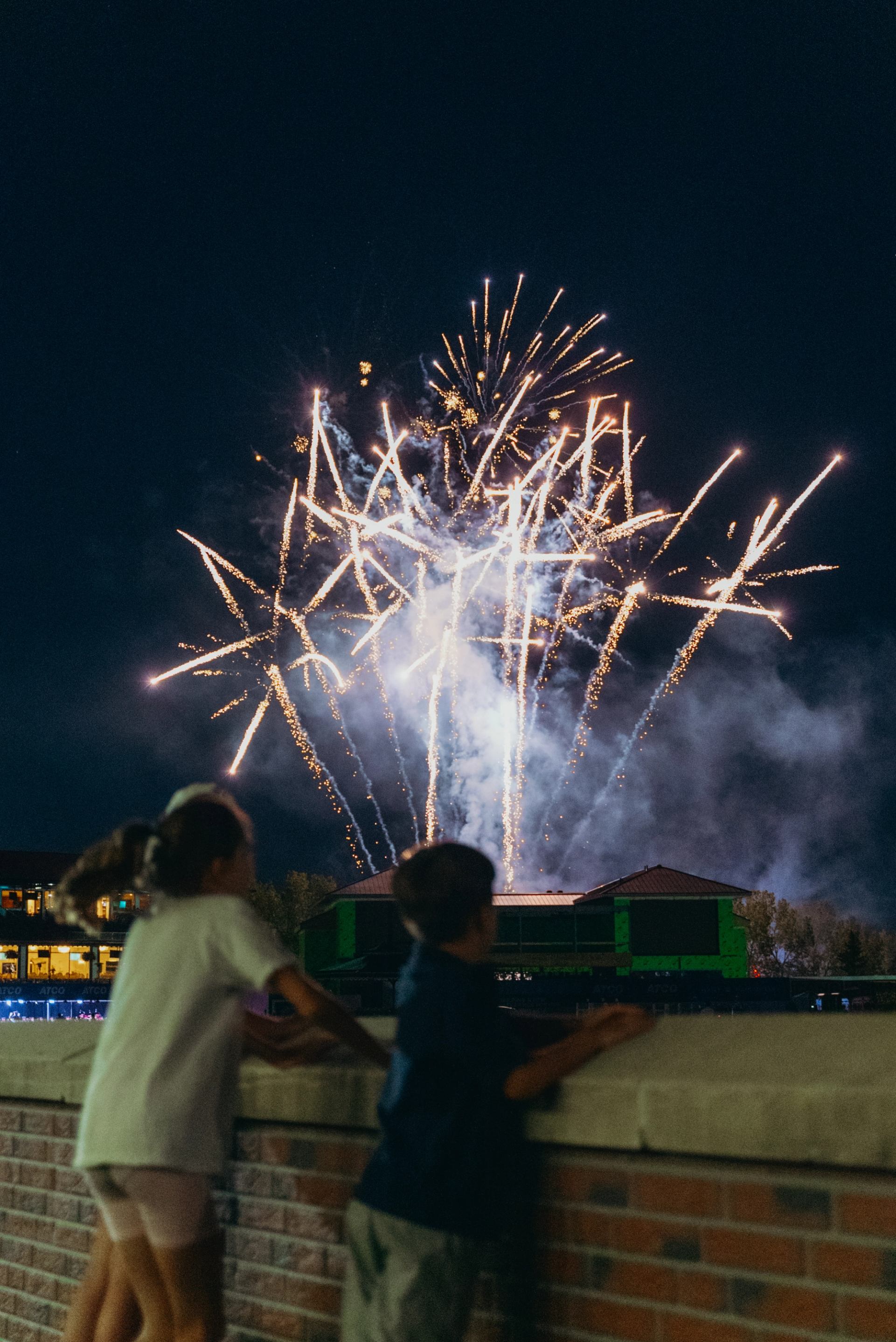 Two children watching fireworks from a brick bridge.