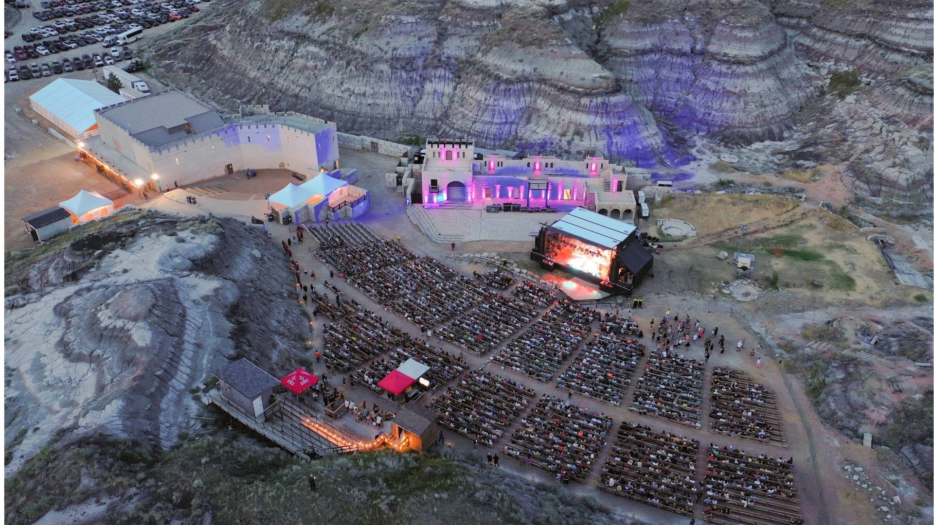Outdoor amphitheatre in rocky canyon with large audience watching illuminated stage performance.