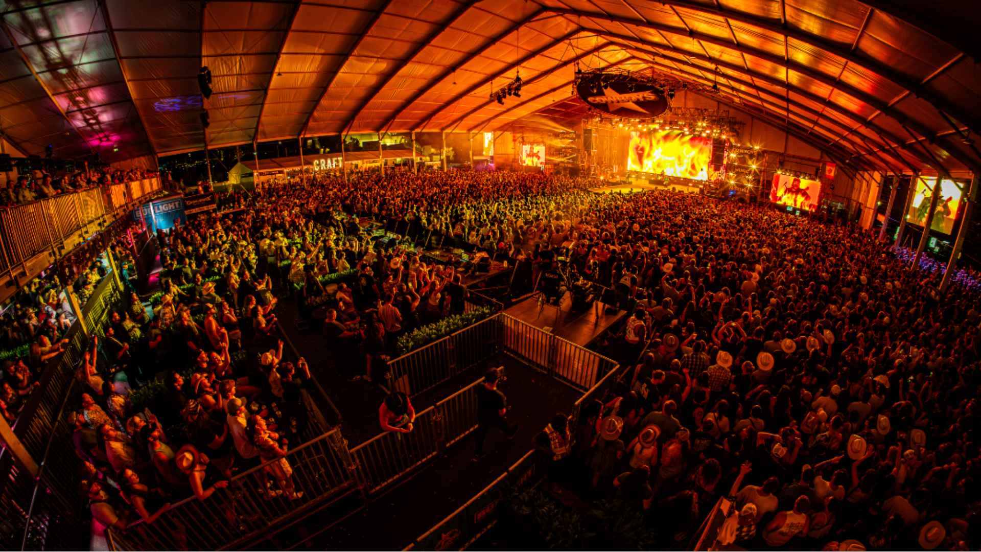 Large crowd at a lively country music concert inside a tent, with a brightly lit stage.