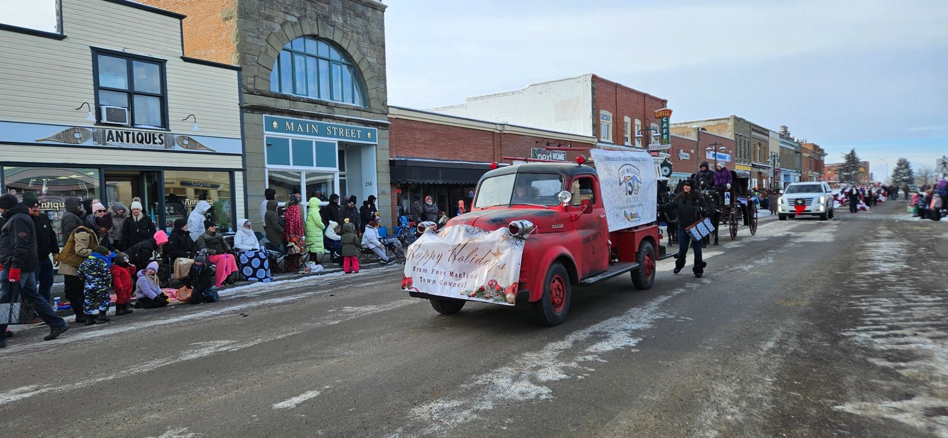 Vintage red fire truck with “Merry Christmas” banner rolls through parade crowd.