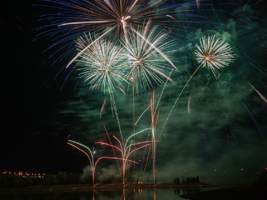Fireworks over a dark sky and a river, with coloured bursts and smoke.