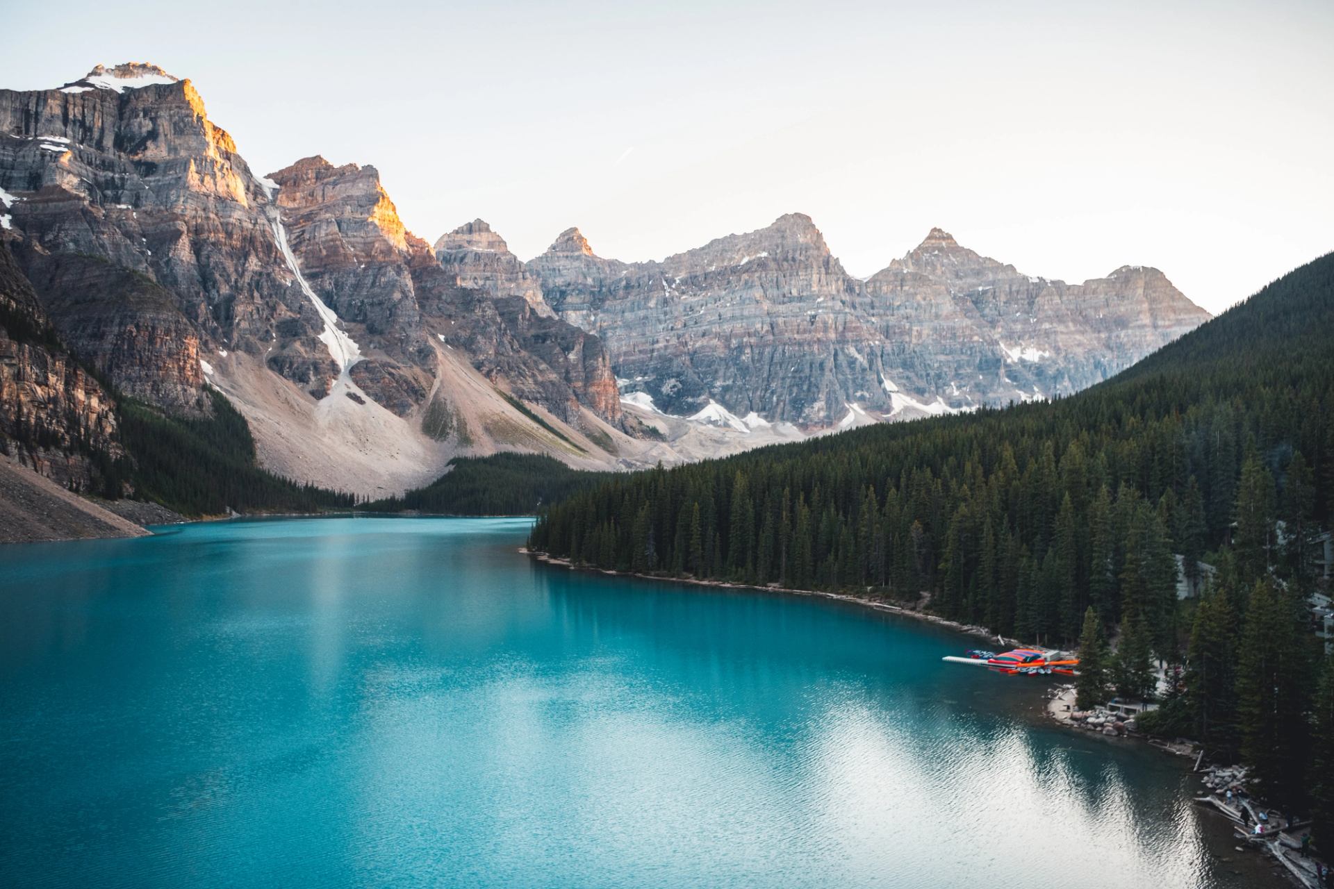 Turquoise mountain lake bordered by dense evergreen forest and rocky peaks with snow patches.