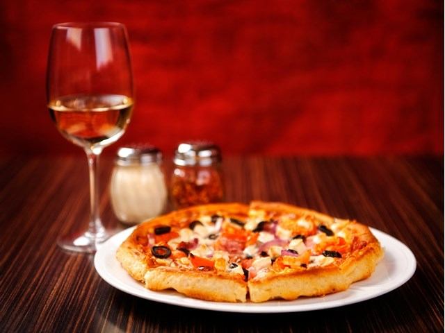 Pizza on white plate with wine glass and shakers on table.