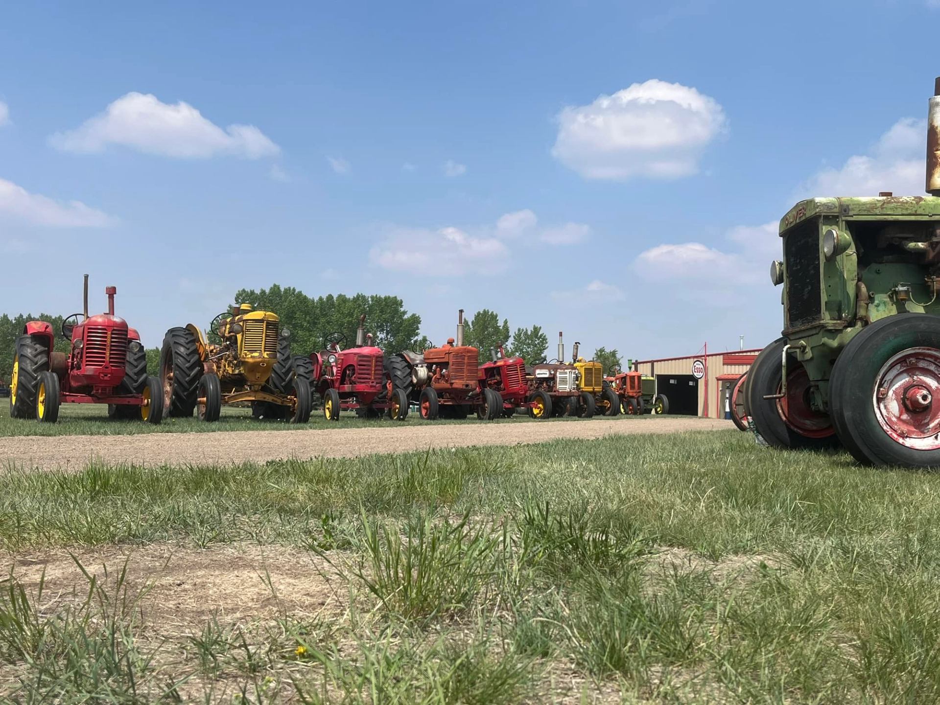 A photo of antique tractors lined up along a gravel road with bluesky behind them