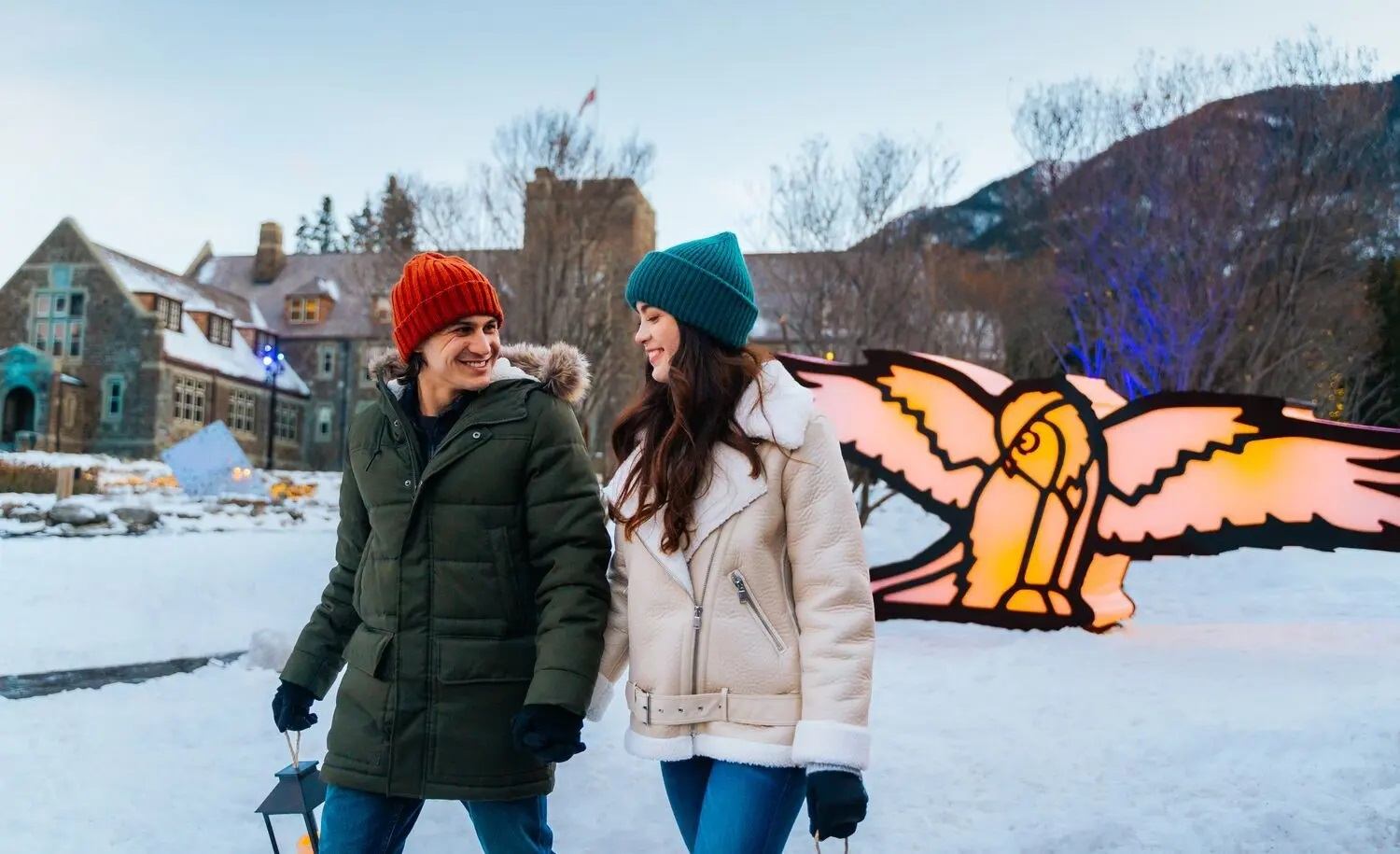 Couple walks hand in hand in snowy setting with glowing owl display at In Search of Christmas Spirit.