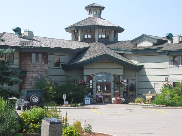 Visitor center with a tower and large windows, surrounded by trees, glowing in sunset light.