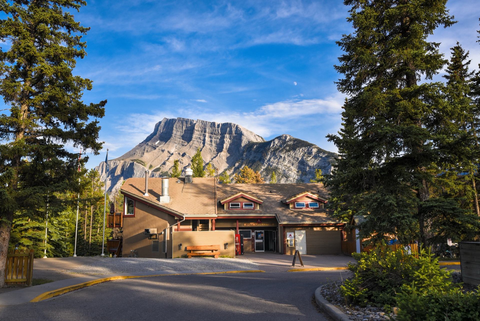 Lodge at HI Banff Alpine Centre with mountain backdrop and tall pine trees.